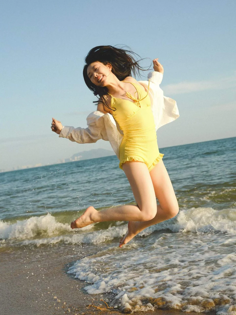 A woman in yellow jumping above the surf with the sea behind her