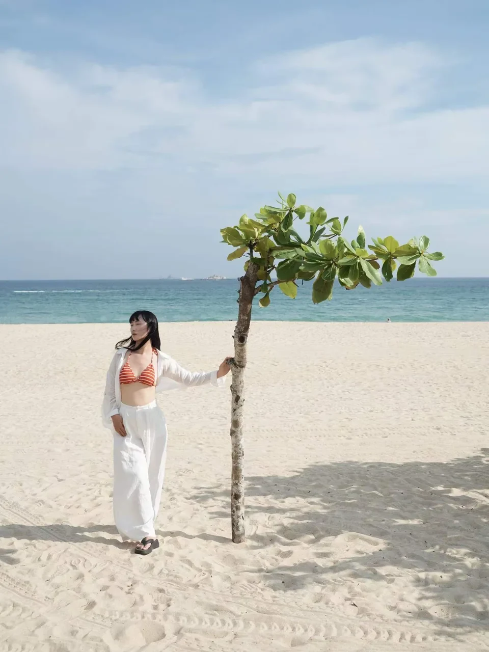 Turquoise sea and pale sand behind a beach tree and a woman at Tianyu in Sanya