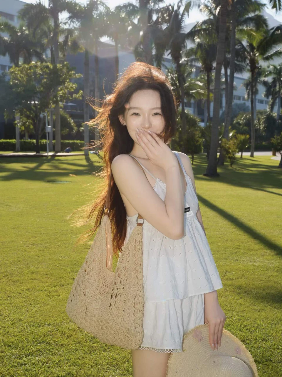 A woman in white on a sunlit lawn with tall palms behind her