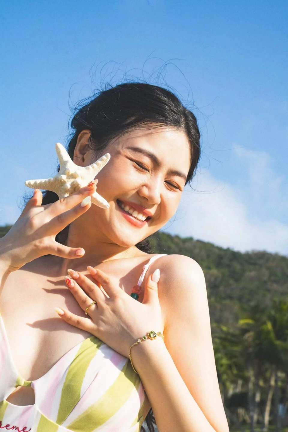 A smiling woman holding a starfish beside her face beneath a blue sky