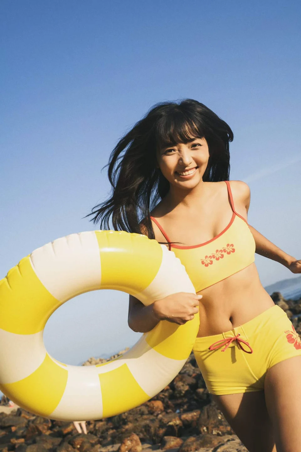 A woman in yellow holding a yellow and white swim ring on a rocky shore